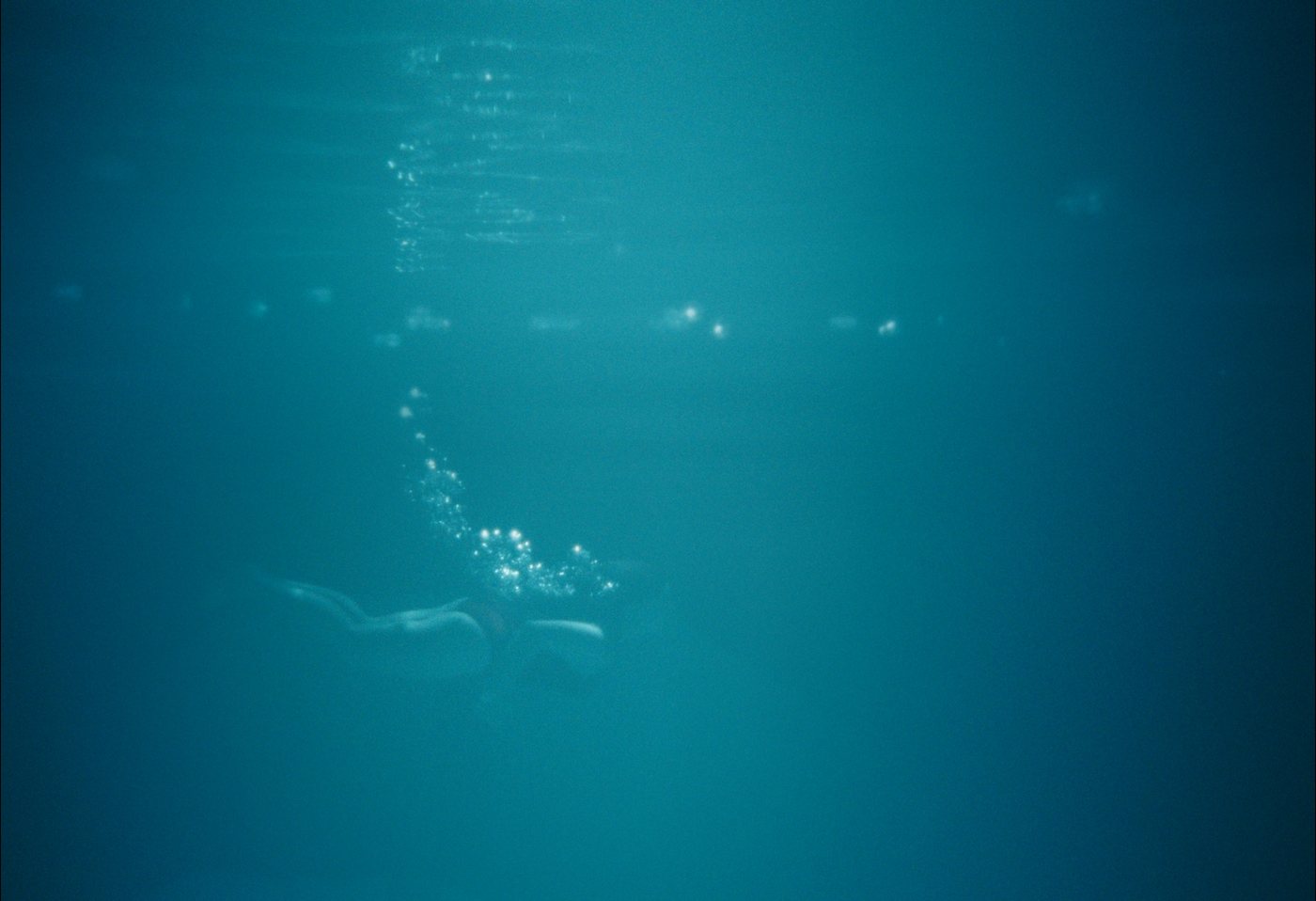 Yasmin swimming underwater, trailing a line of bubbles.